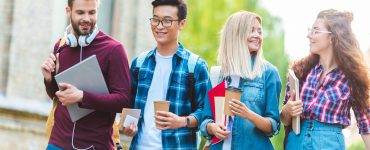 portrait of smiling multiethnic students with backpacks walking in park